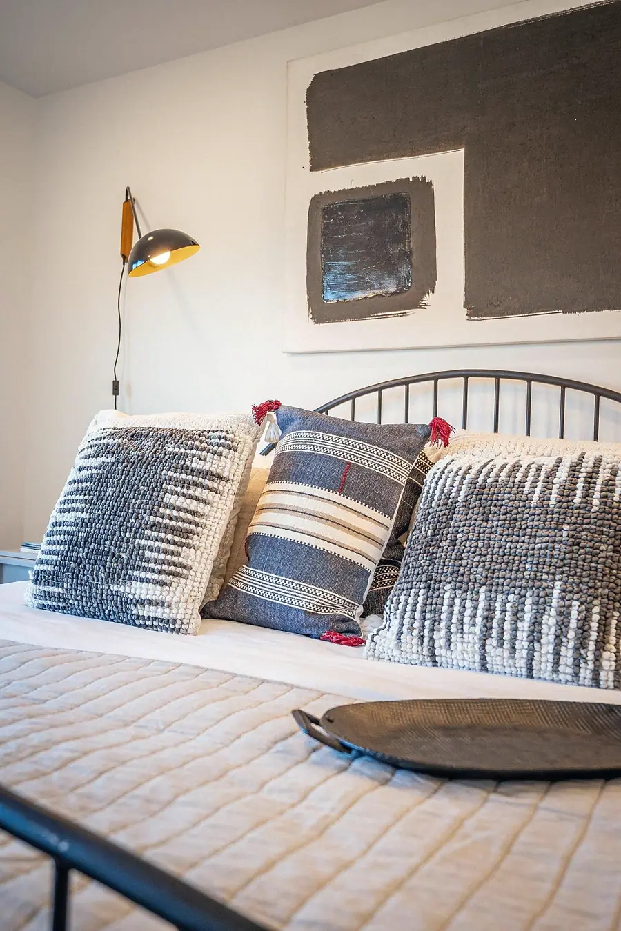 Silver Creek bedroom detail with textured pillows, black tray, and wall sconce