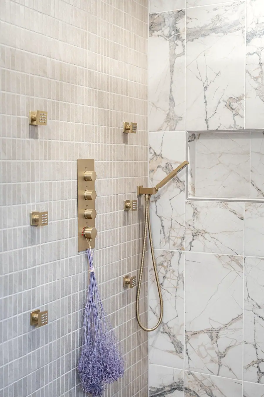 Grand Vista shower controls with brass fixtures, hand shower, and marble niche
