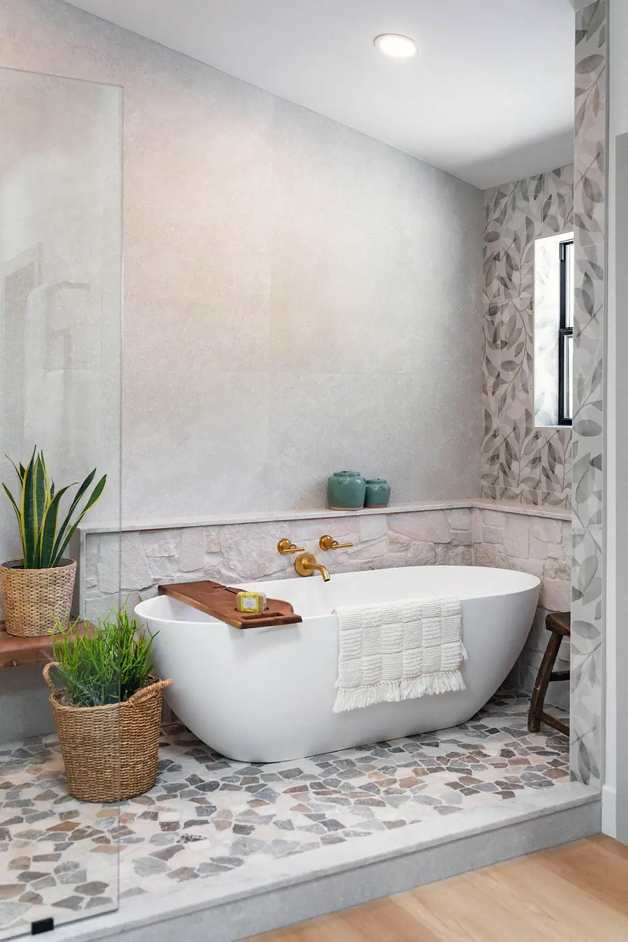 Little Gem freestanding tub with brass fixtures, stone ledge, and leaf-pattern tile