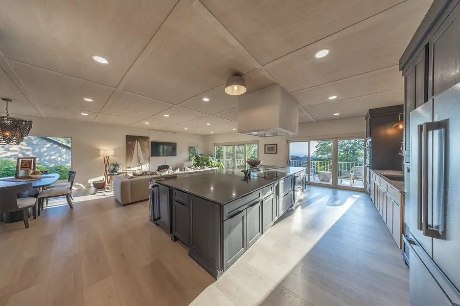 Open kitchen, dining, and living with charcoal island, wood ceiling, and mountain-view doors