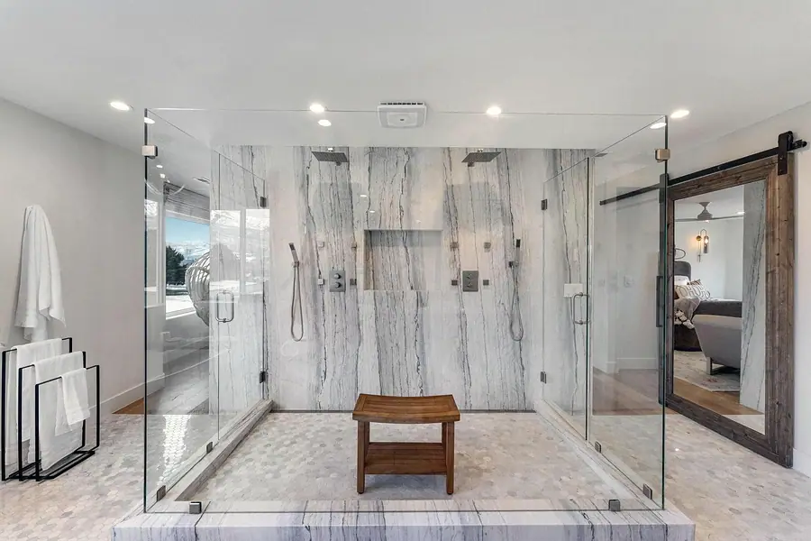 Dual rain shower with marble walls, teak stool, and barn-door mirror