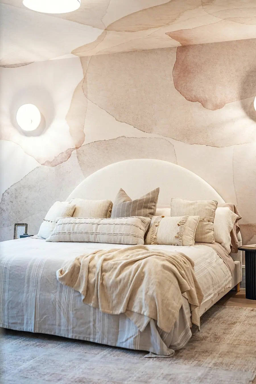 Grand Vista primary bed with layered linen pillows, beige throw, and abstract mural wall