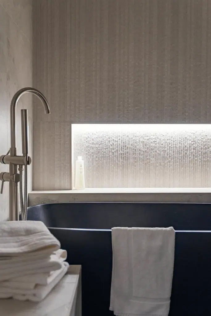 Crista da Montanha black soaking tub detail with backlit fluted niche and stacked white towels