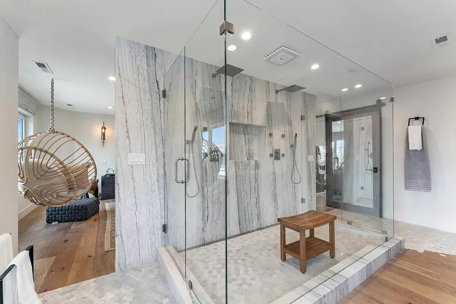 Glass shower with marble walls looking toward hanging chair and suite