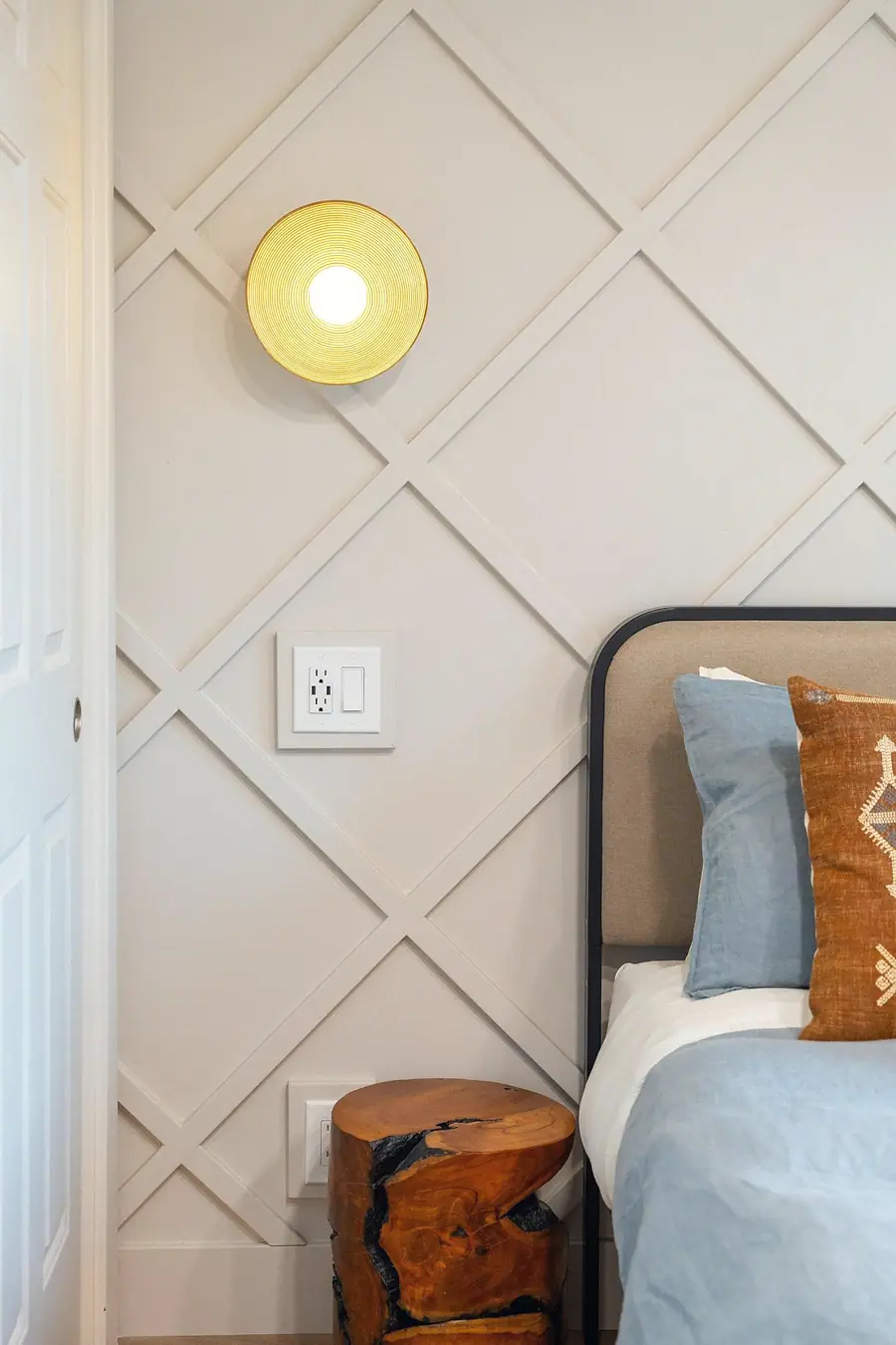 Midway bedroom detail with gold disc sconce, diamond molding, and live-edge stump table