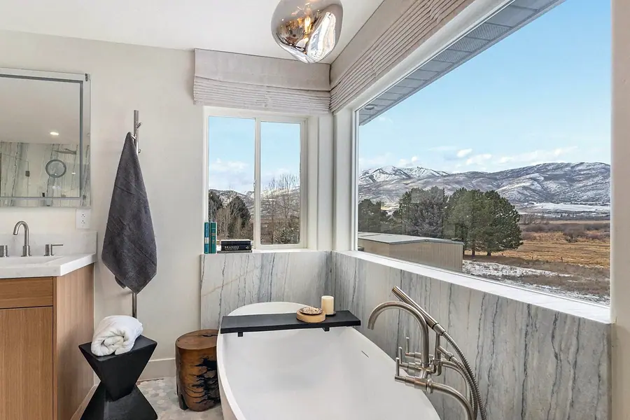 Primary bath tub and vanity with floor-to-ceiling mountain views