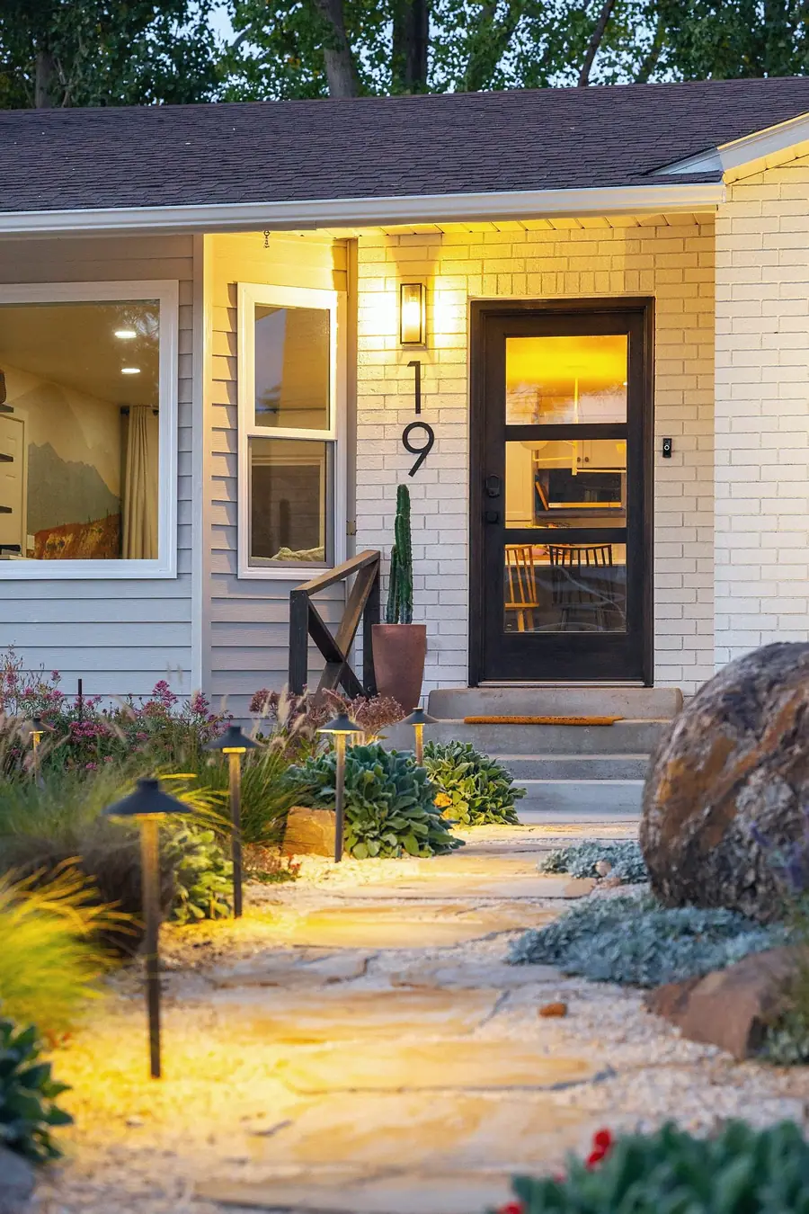Midway front entry at dusk with path lights, cactus planter, and glowing interior