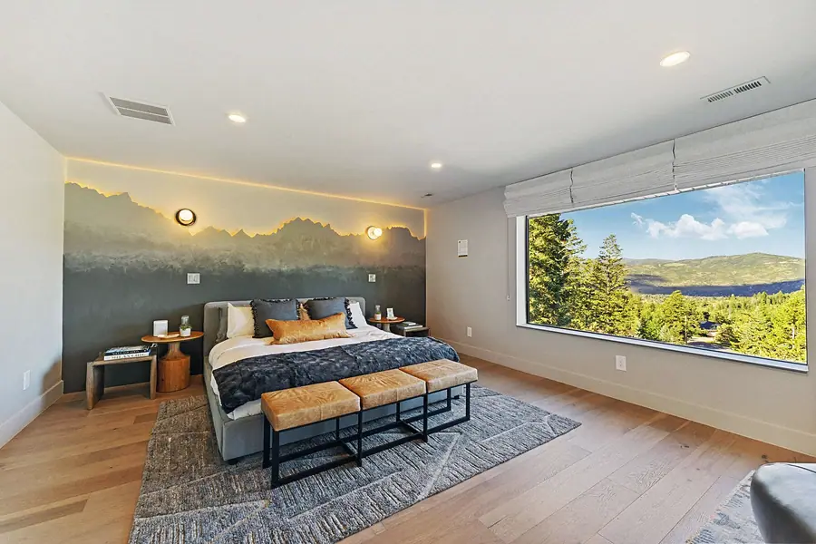 Matterhorn Hygge House primary bedroom with mountain mural wall, leather bench, and forest window view