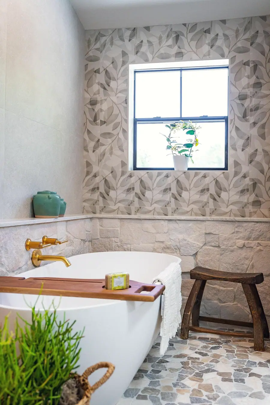 Little Gem bathtub corner with leaf wallpaper, window plant, and rustic wood stool
