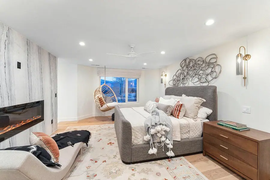 Primary bedroom with grey upholstered bed, hanging chair, and fireplace