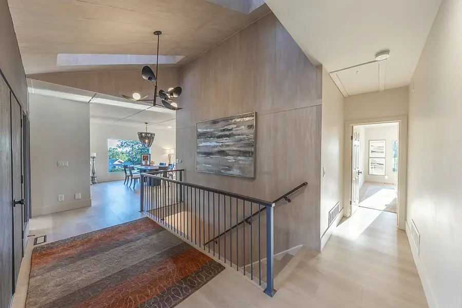 Upper hallway with warm wood paneling, metal stair rail, and view into the dining room
