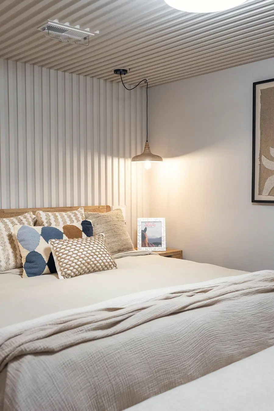 Midway bedroom detail with textured pillows, pendant light, and neutral bedding