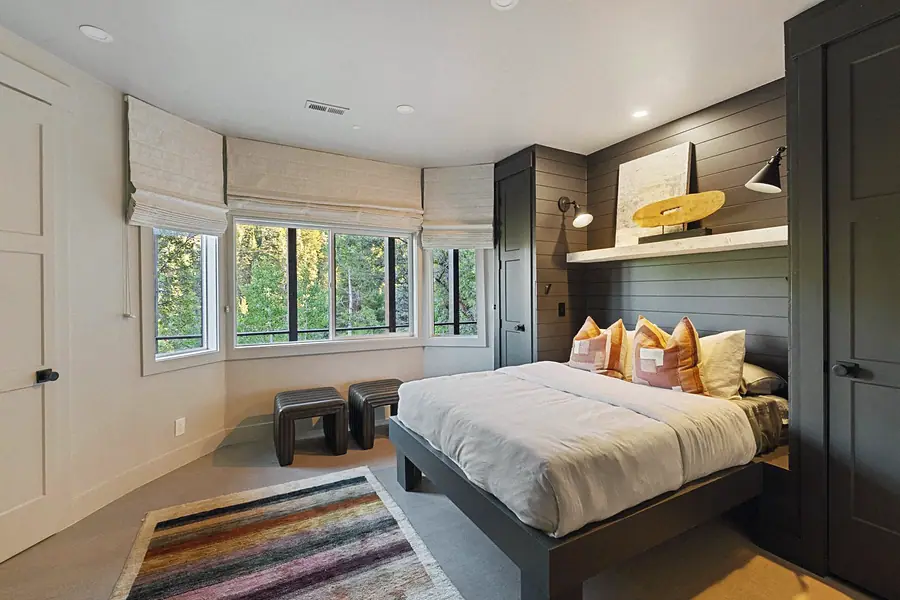 Matterhorn Hygge House bedroom with dark shiplap wall, platform bed, and forest bay windows