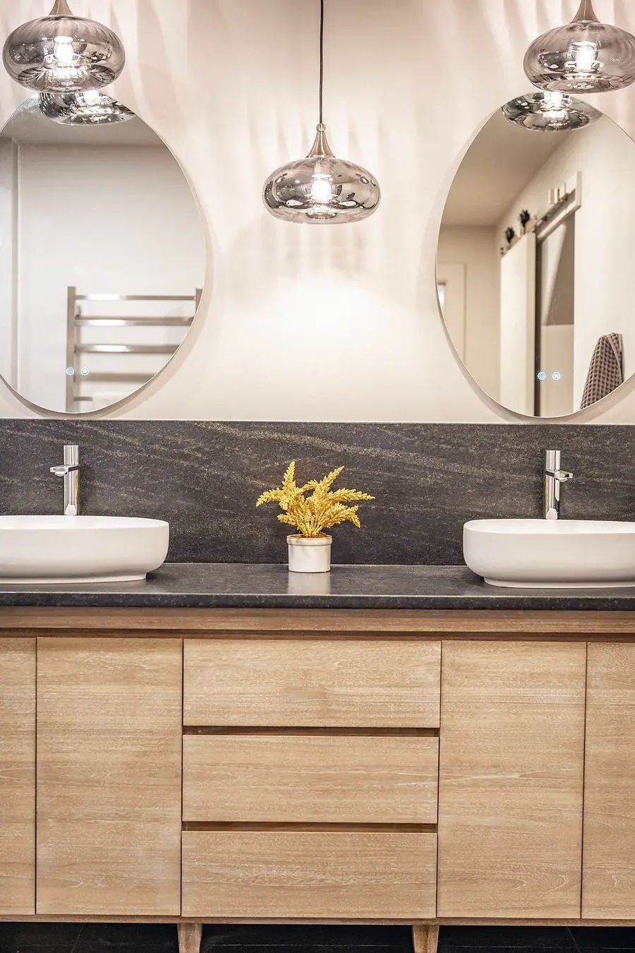 Grand Vista double vanity with round mirrors, glass pendants, and light oak cabinets