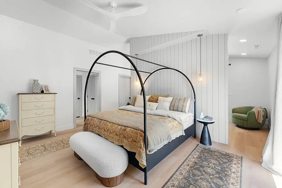 Little Gem primary bedroom with black arched canopy bed, white bouclé bench, and green lounge chair