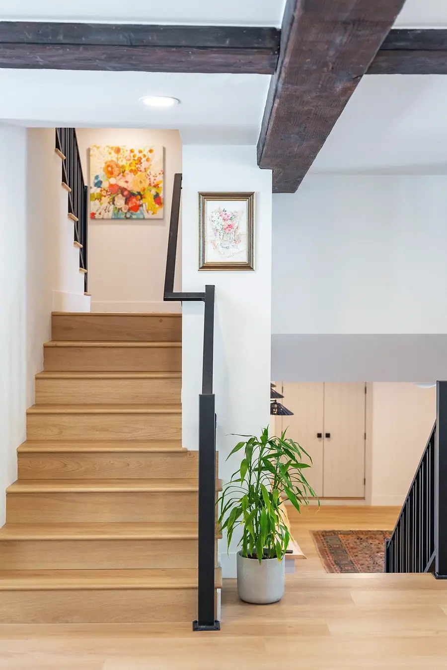 Little Gem oak staircase with black rail, floral art, and potted plant