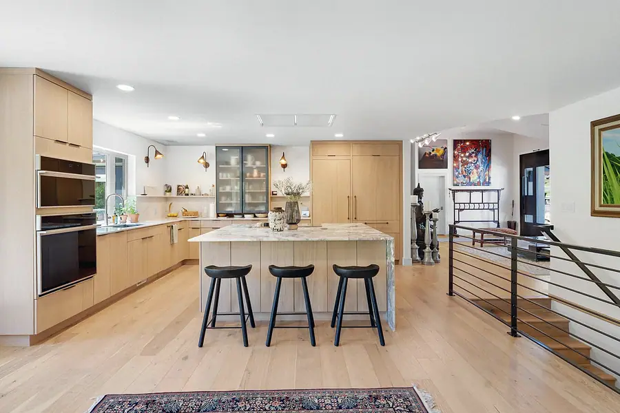 Elysium kitchen island with black stools, glass-front cabinets, and entry hall beyond