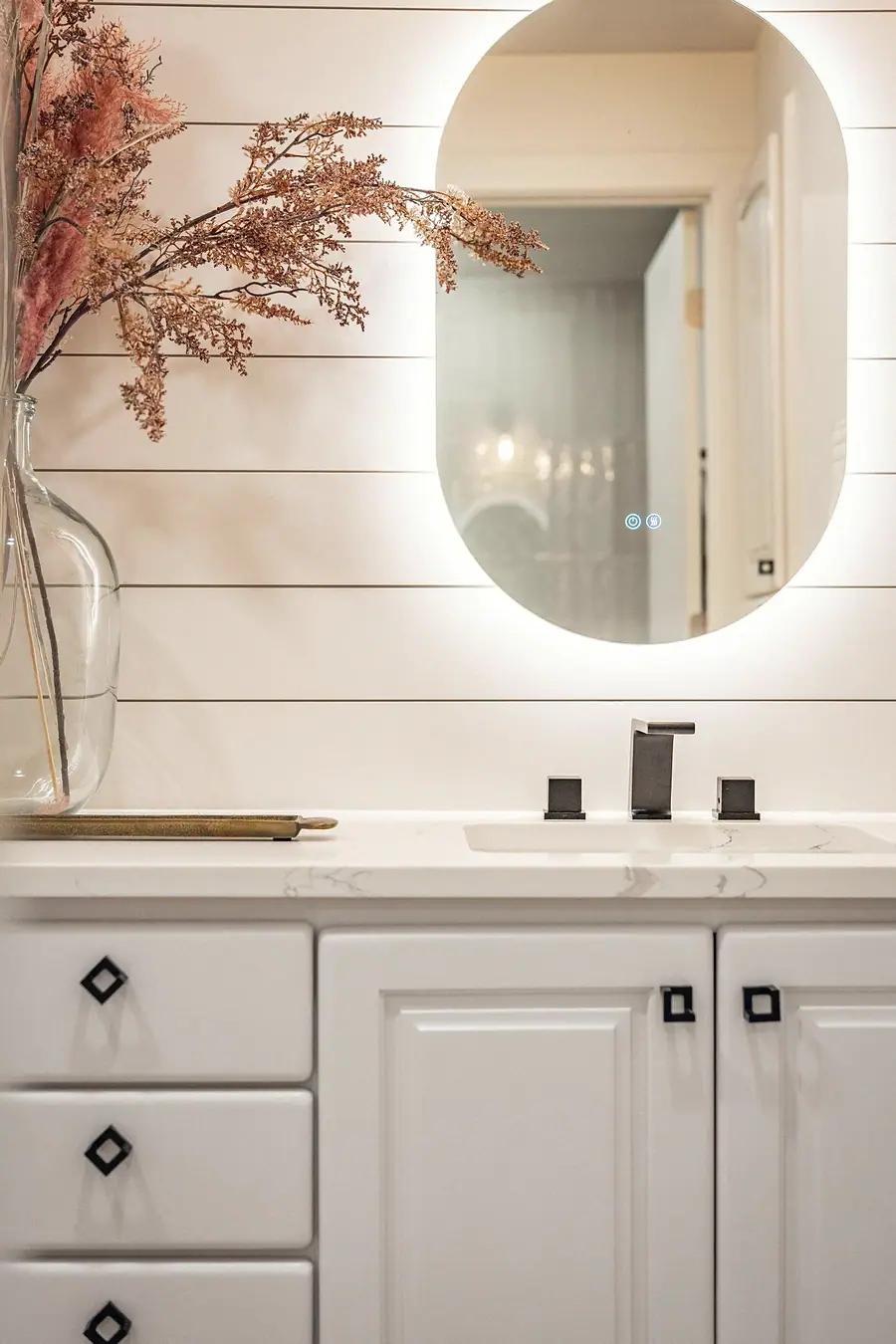 Grand Vista vanity detail with backlit oval mirror, black faucet, and dried florals