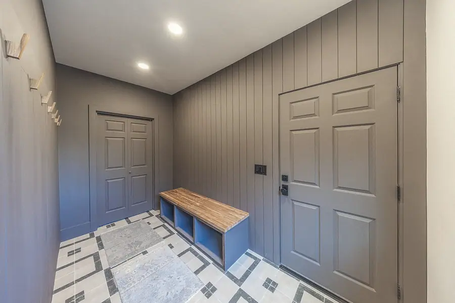 Mudroom with gray board-and-batten walls, wood bench, and patterned tile floor