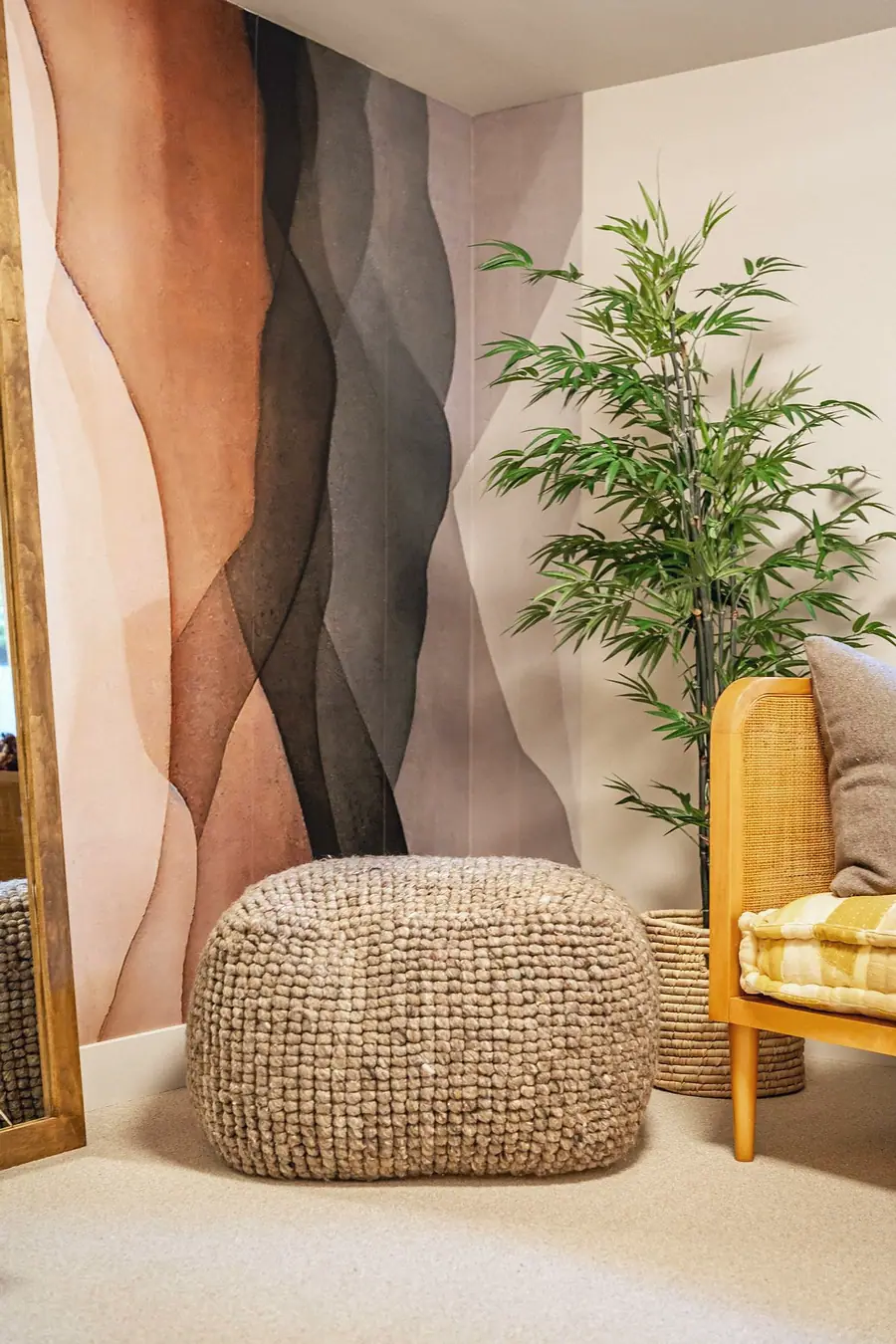Grand Vista corner with abstract mural wall, knotted wool pouf, bamboo plant, and cane chair