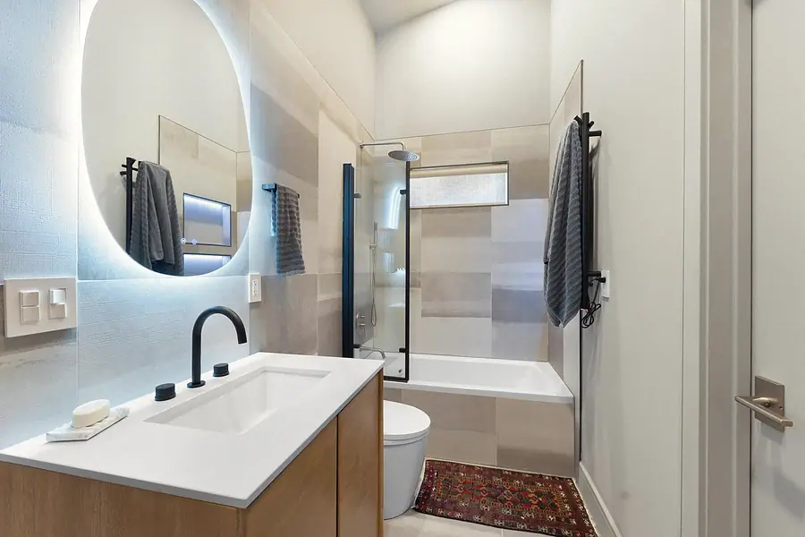 Elysium bathroom with backlit round mirror, wood vanity, and glass shower