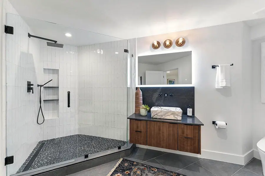 Bath with glass shower, pebble floor, floating wood vanity, and marble vessel sink