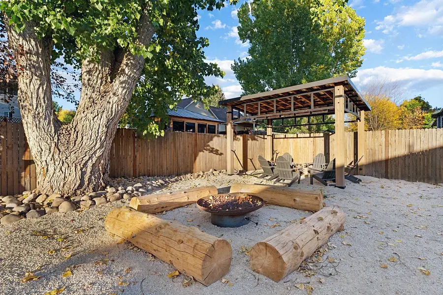 Midway fire pit with log seating under a large tree and wood pergola beyond