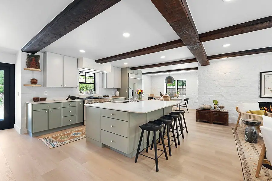 Little Gem kitchen with sage island, black stools, and dark wood ceiling beams