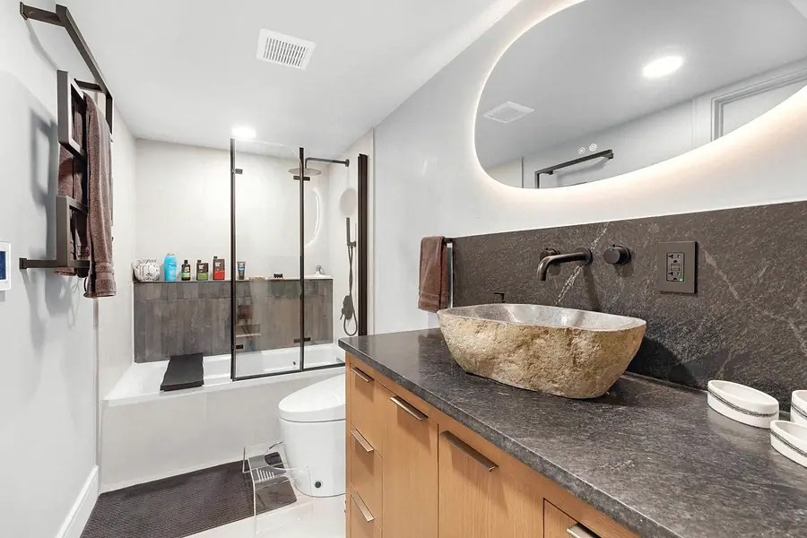 Elysium bath with stone vessel sink, dark stone counter, and glass tub shower