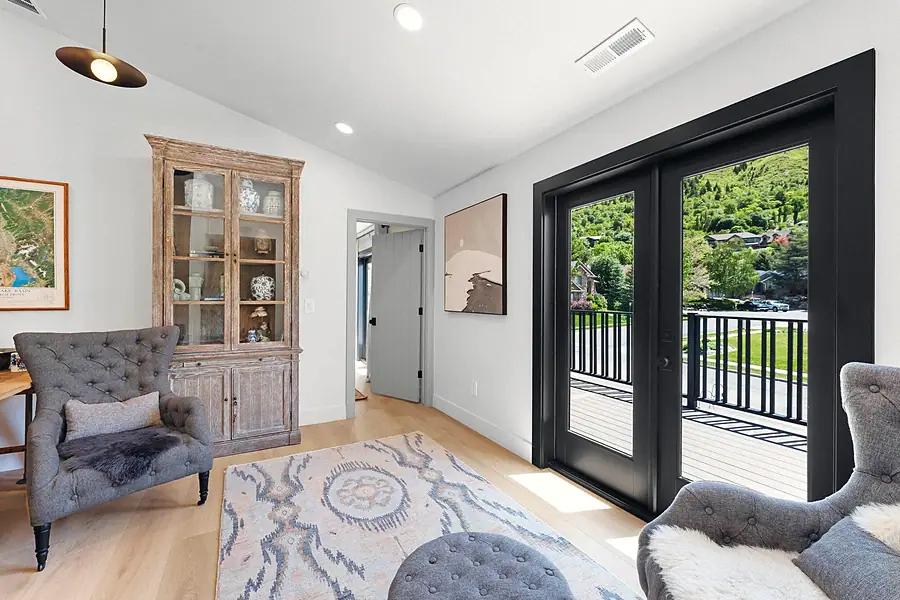 Little Gem sitting room with tufted gray chairs, antique hutch, and black French doors to the deck