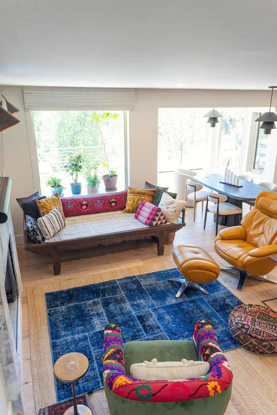 Elysium living room daybed by the window with colorful textiles, blue rug, and dining beyond
