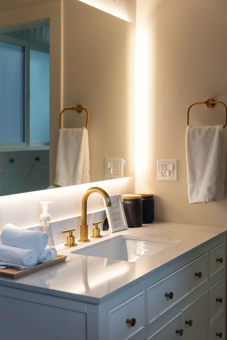 Midway vanity detail with backlit mirror, brass faucet, and rolled white towels