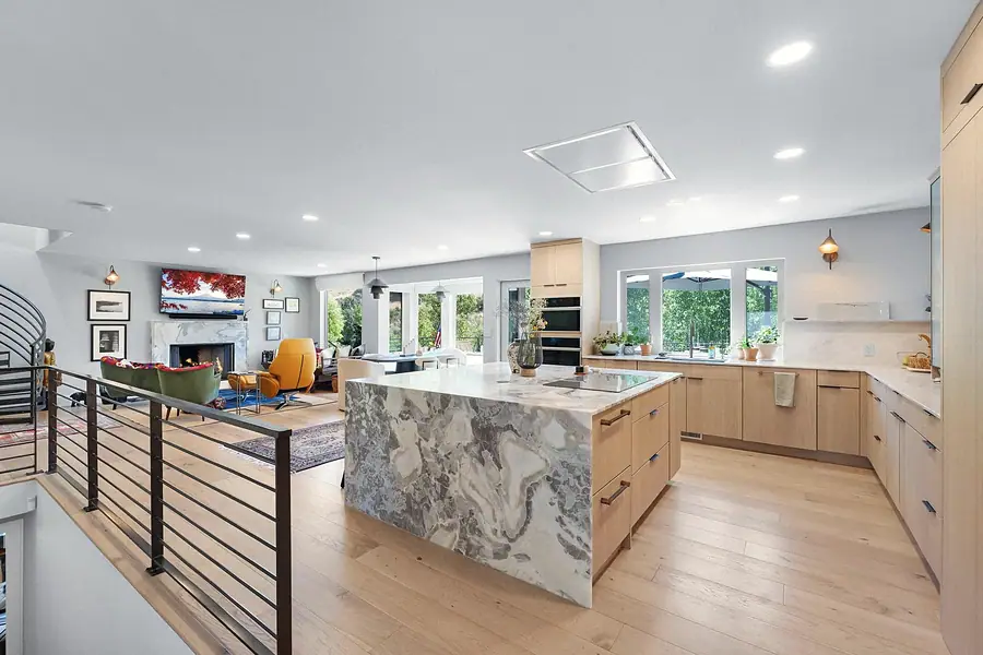 Elysium open kitchen and living area with marble waterfall island, light oak cabinets, and fireplace lounge